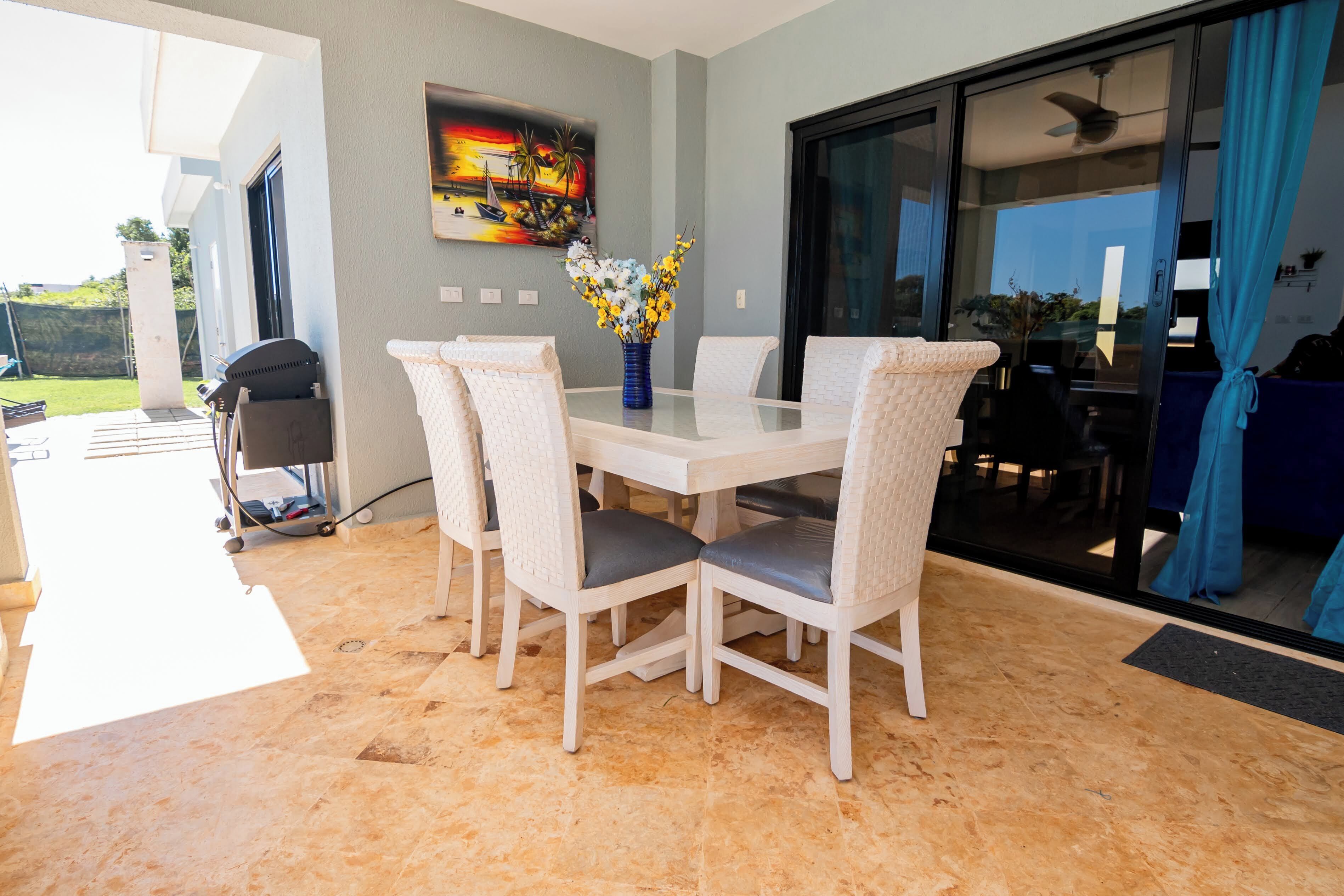 Un coin repas avec une table en verre, des chaises blanches et un vase de fleurs.