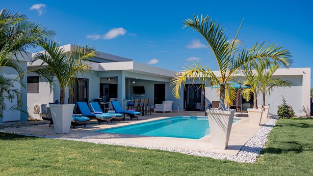 A modern house with a swimming pool, lounge chairs, and palm trees.