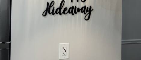 A wall with a decorative sign saying "the happy sideaway" and a modern pendant light.