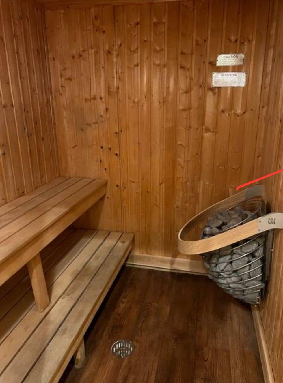 A wooden sauna with benches and a stone-filled container, likely for heating.