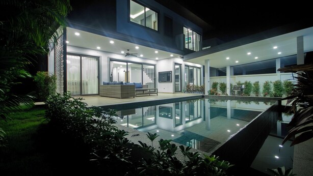A modern house with a swimming pool, large windows, and a well-lit interior.