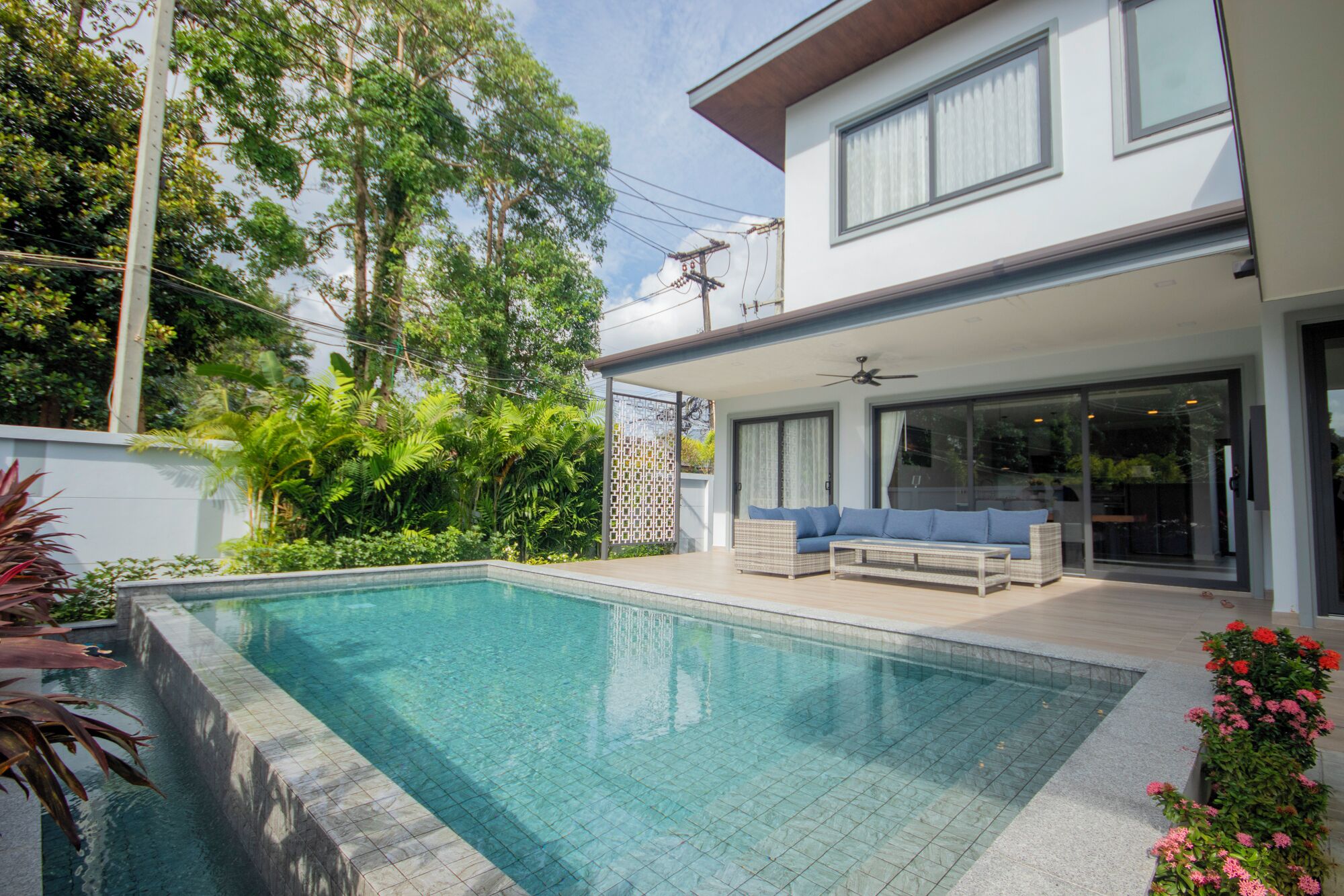 A modern house with a swimming pool, a covered patio with outdoor furniture, and lush greenery.