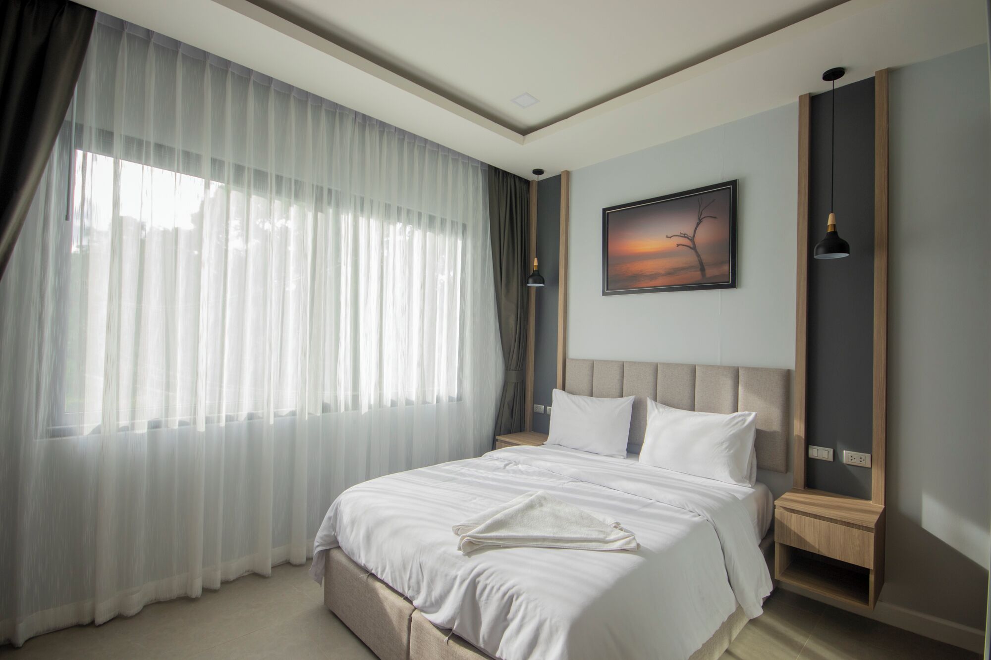 A modern hotel room with a large bed, a nightstand, a bedside lamp, and a painting on the wall.