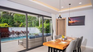 A modern dining area with a large glass wall, a pool, and a sunset view.