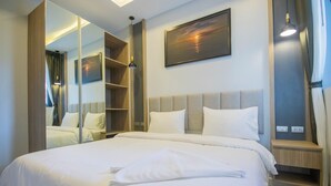 A hotel room with a large bed, a bedside table, a mirror, a painting on the wall, and a window with curtains.