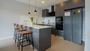 A modern kitchen with a central island, bar stools, a refrigerator, and a microwave.