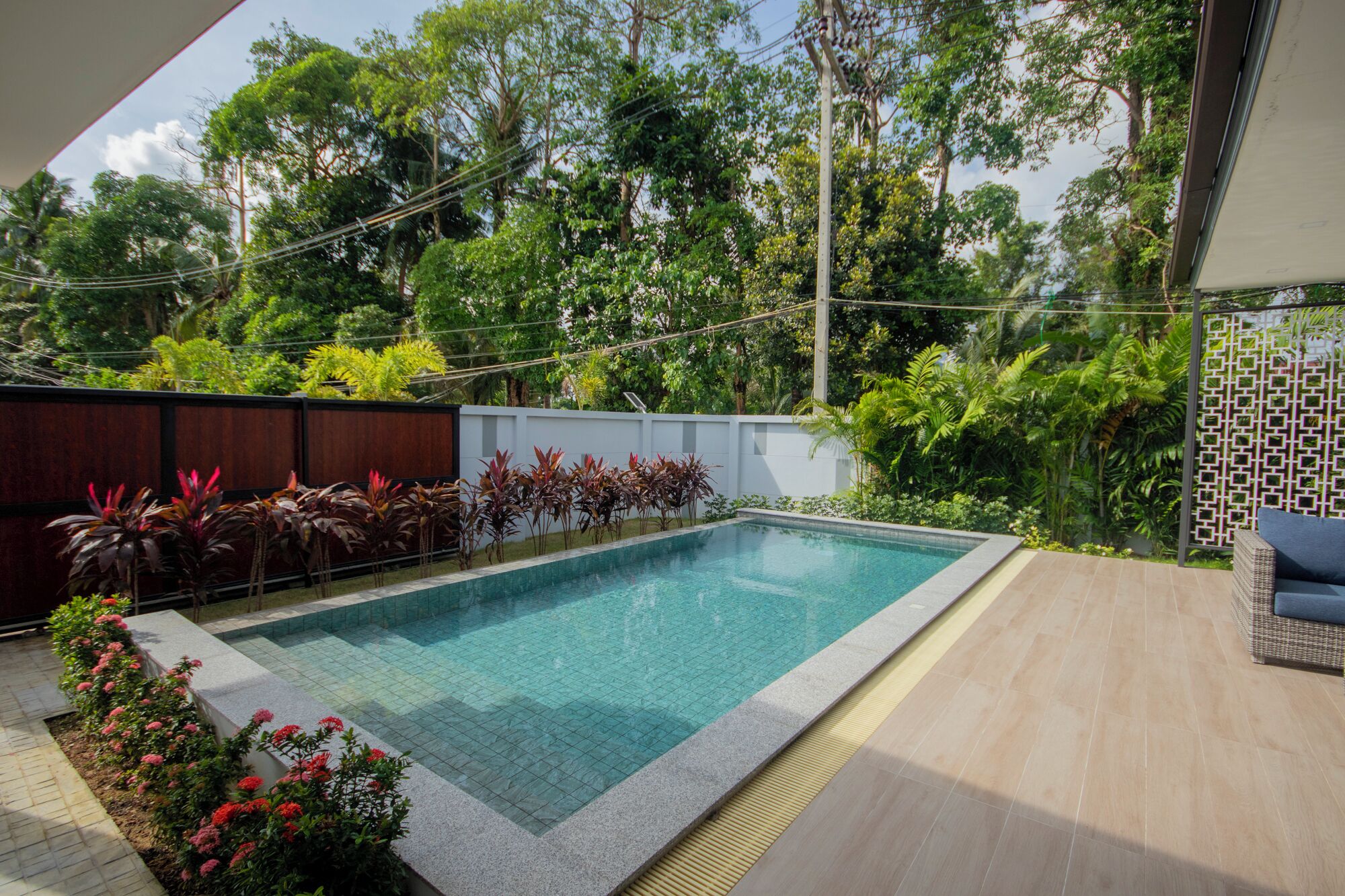 A rectangular swimming pool with a tiled edge, surrounded by a wooden deck and a low wall.
