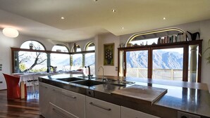 Une cuisine moderne dotée d’un grand îlot central, d’appareils électroménagers intégrés et offrant une vue sur les montagnes grâce à de grandes fenêtres.