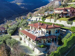 A hillside residential area with a prominent house featuring a red-tiled roof, a stone staircase, and a patio with outdoor furniture. - Beautiful apartment for 8 people with WIFI, TV, terrace and pets allowed (Riva Di Solto)