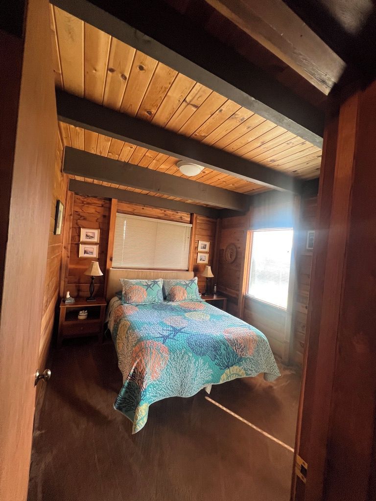 A wooden cabin bedroom with a bed, two bedside tables, and a window.