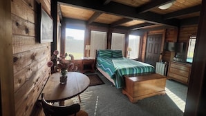 A cozy cabin-style room with a wooden interior, a bed with a green and blue striped bedspread, a wooden nightstand, a round table with a vase of flowers, and a dresser with a television. - Ocean View, Cozy 2-bedroom cabin in tranquil Gualala with WiFi and huge firepit (gualala)