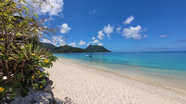 A beach with clear turquoise water, a boat, and a mountain in the background. - Private house located 100 meters from the beach (Fare)