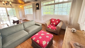 A cozy living room with a grey sofa, a wicker chair with a red cushion, and a small table with a decorative item. - Private house located 100 meters from the beach (Fare)