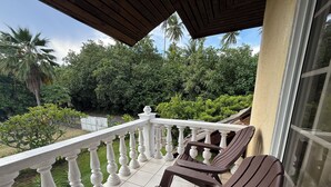 A balcony with two brown chairs, a white balustrade, and a view of lush greenery and palm trees. - Private house located 100 meters from the beach (Fare)