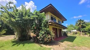 A two-story house with a red roof, surrounded by lush greenery and a well-maintained lawn. - Private house located 100 meters from the beach (Fare)