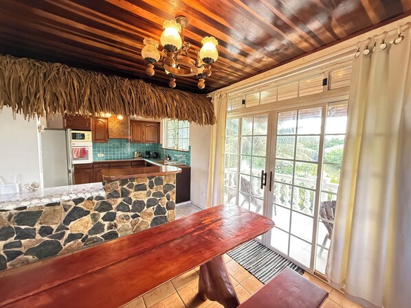 Una cocina con una isla de piedra, techo de madera y vistas a través de puertas de vidrio.