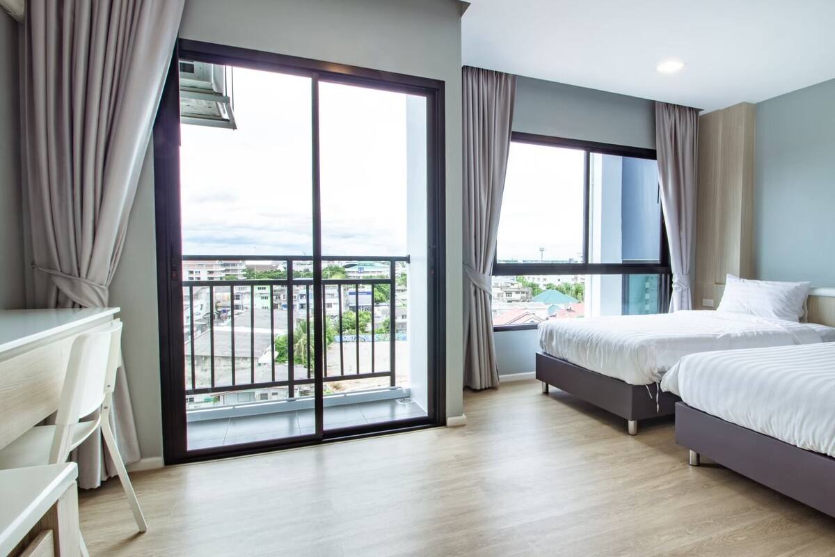 A hotel room with a balcony, two beds, a desk, and a view of the cityscape.
