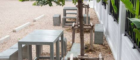 Outdoor seating with concrete tables and benches, a wooden climbing structure, and a white fence.