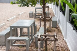 Mobiliario exterior con mesas y bancos de hormigón, una estructura de madera para escalar y una valla blanca.
