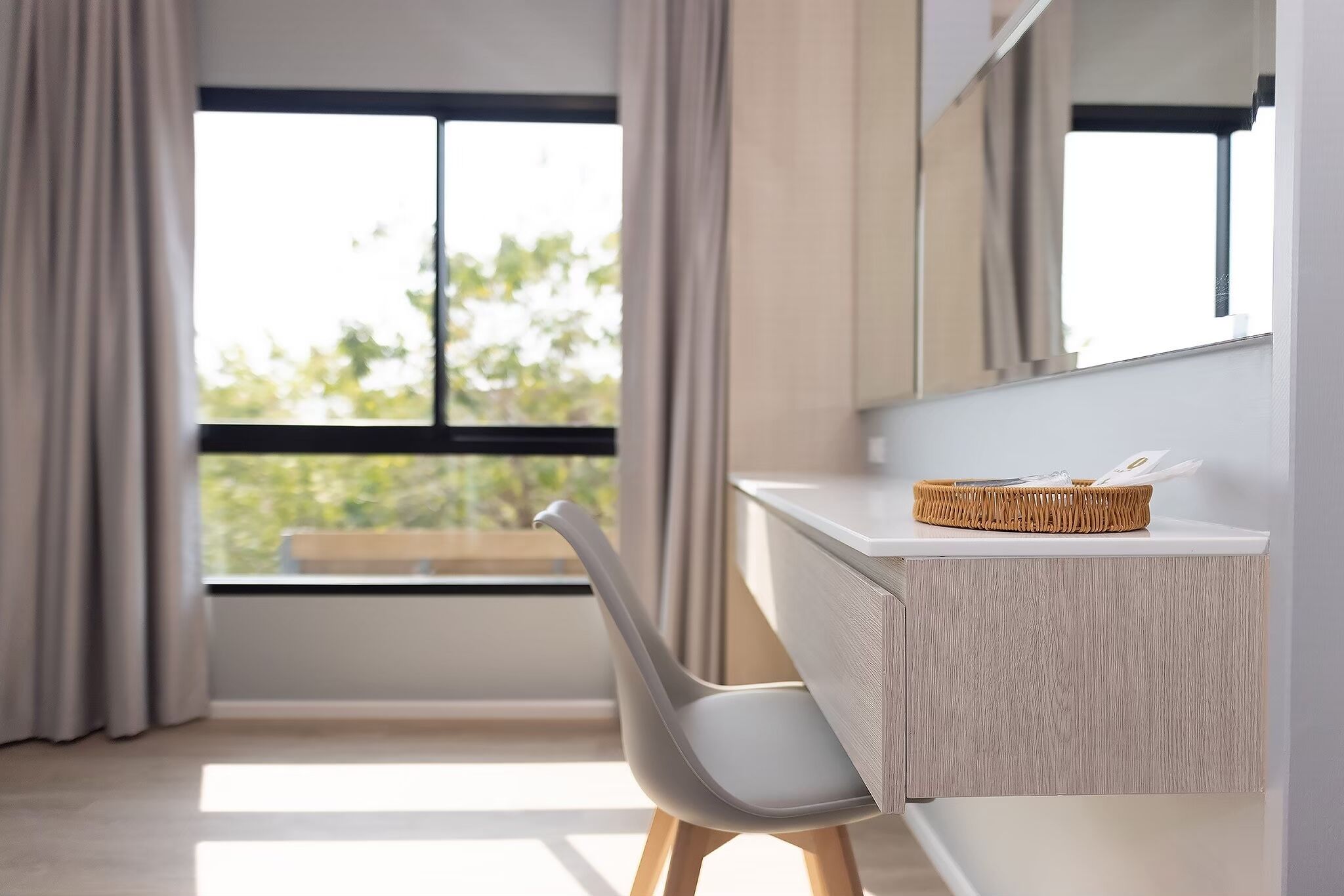 Una habitación moderna con un ventanal grande, una silla blanca y un escritorio de madera con una cesta encima.