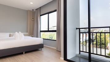 Un dormitorio moderno con una cama grande, vistas de la ciudad a través de amplios ventanales y un balcón con barandilla.