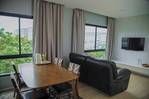 A modern living room with a wooden dining table, black leather sofa, and a TV mounted on the wall.
