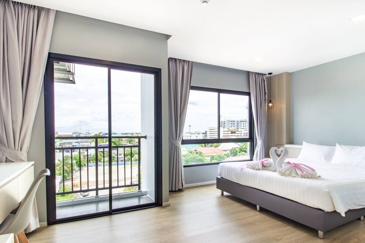 A modern hotel room with a bed, a desk, and a balcony with a city view.
