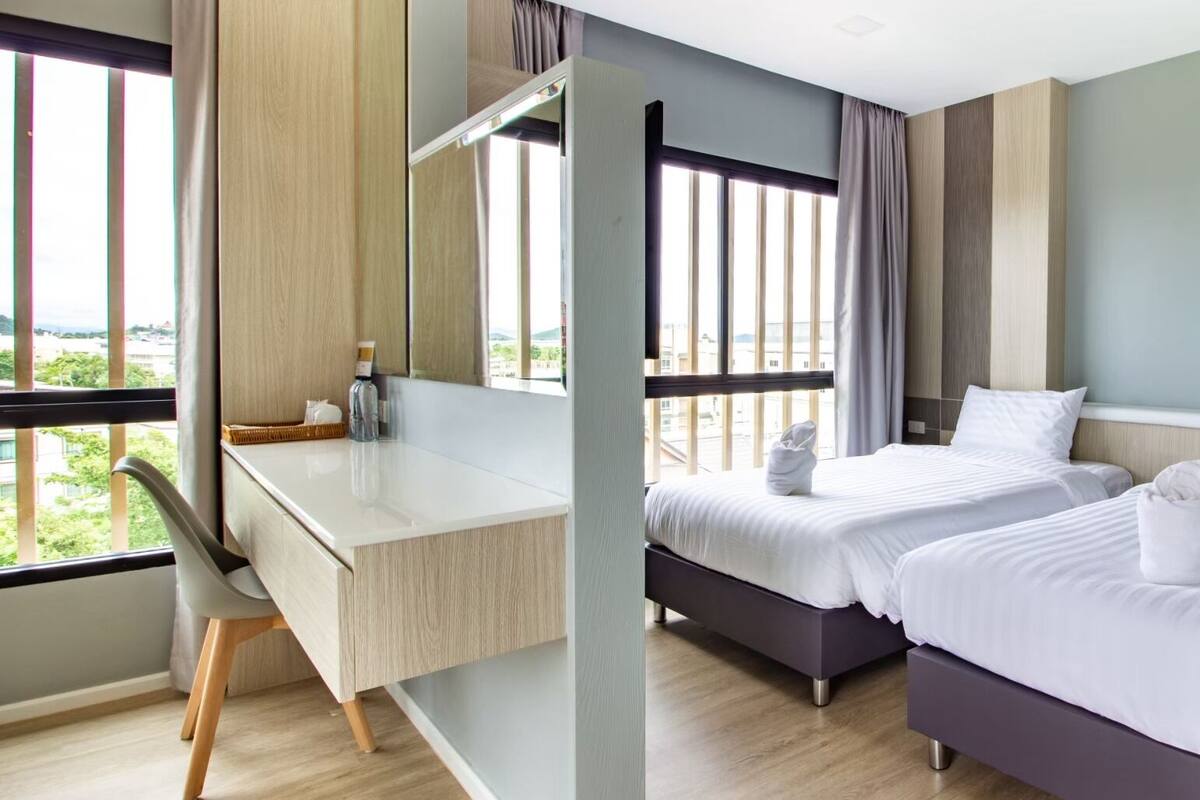 A hotel room with a desk, two beds, a large window, and a view of the outdoors.
