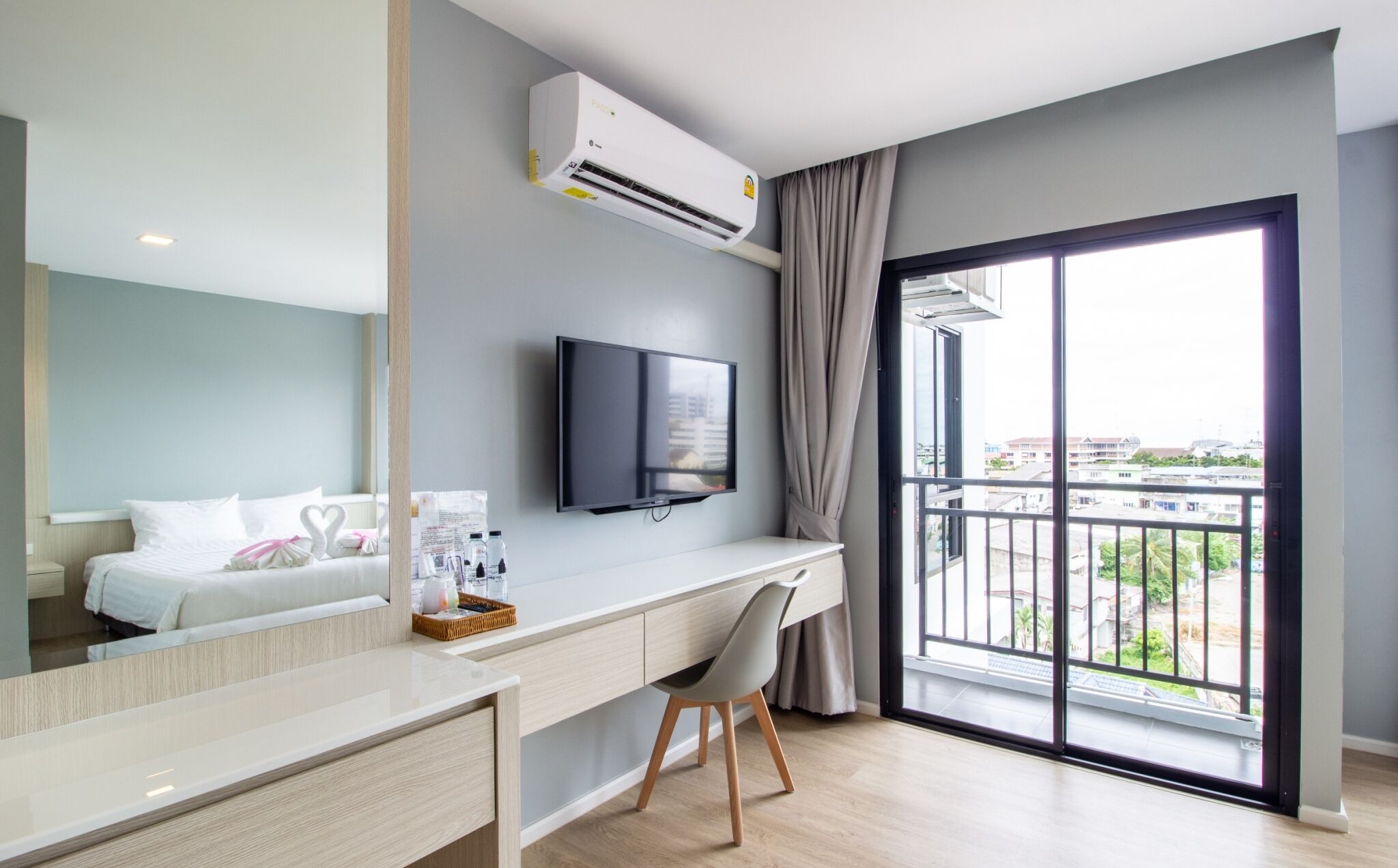 A hotel room with a bed, a desk with a chair, a flat-screen TV, and a large window with a view of buildings.