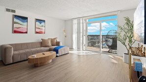 A modern living room with a sofa, a coffee table, and a large window with a city view. - Oceanfront Oasis: Serene 1bd Retreat in MDR/Venice (Marina del Rey)