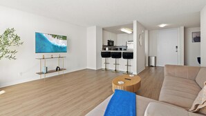 A modern living room with a sofa, a coffee table, and a TV on the wall. There is a kitchen area with cabinets and a microwave. - Oceanfront Oasis: Serene 1bd Retreat in MDR/Venice (Marina del Rey)