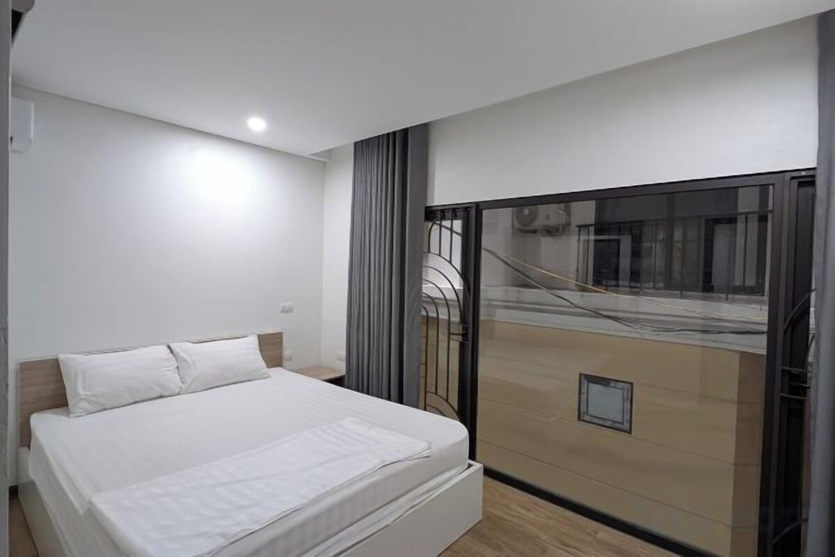Una camera da letto moderna con un letto grande, una porta scorrevole in vetro che dà su un balcone e vista sulla strada.