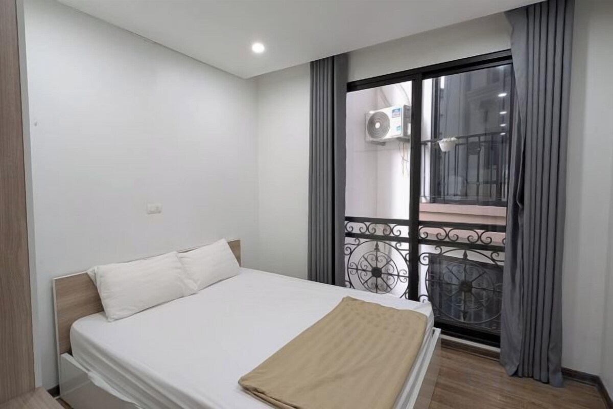 A bedroom with a bed, a window with a view of a balcony, and an air conditioning unit.