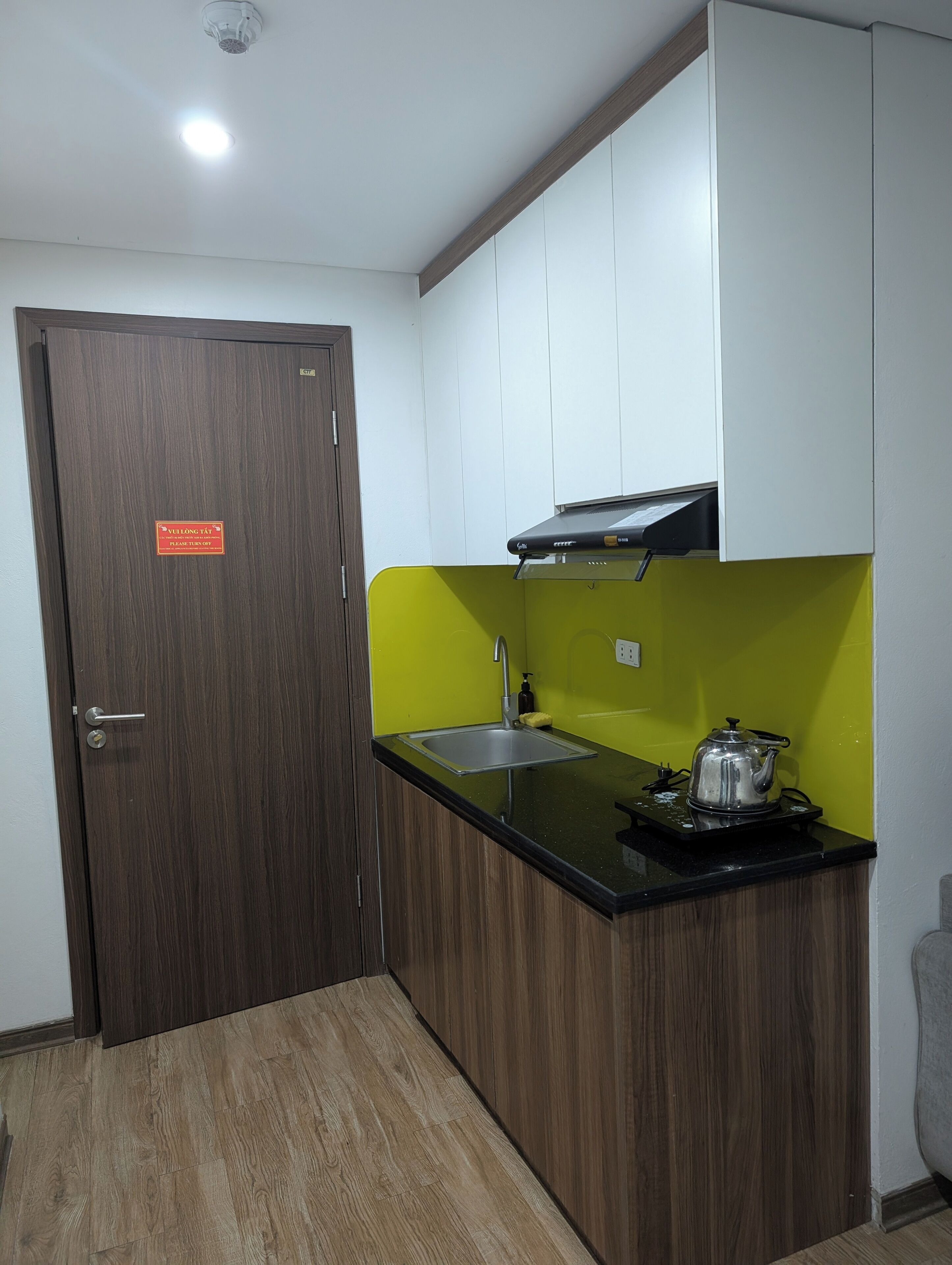 A compact kitchen with a wooden door, a sink, a kettle, and a bright green accent wall.