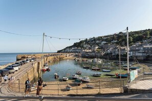 A coastal town with a harbor filled with boats, a promenade with people walking, and houses on a hillside.