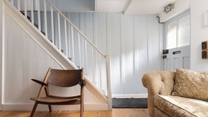 Eine Treppe mit weißen Geländern, ein Holzstuhl und ein beiges Sofa in einem Raum mit Holzboden und weißen Wänden.