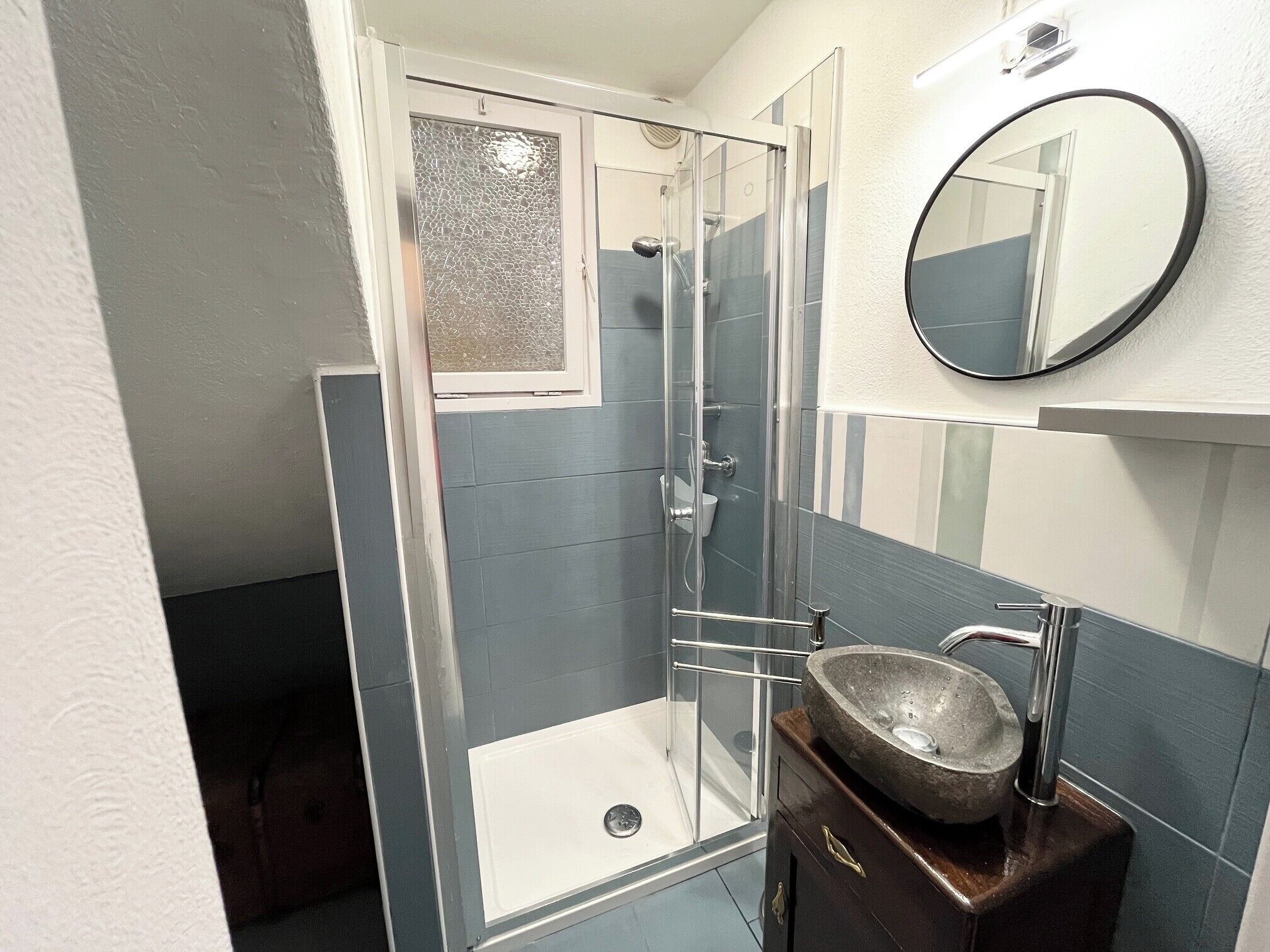 A bathroom with a glass shower enclosure, a sink with a stone basin, and a mirror on the wall.