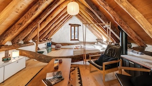 Une chambre mansardée chaleureuse avec un plafond en pente, des poutres en bois, une grande fenêtre, un lit en bois, un bureau et une chaise.