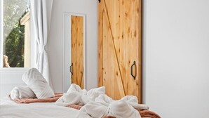 Un dormitori amb llit, tovalloles blanques, un armari de fusta i una finestra amb cortines.
