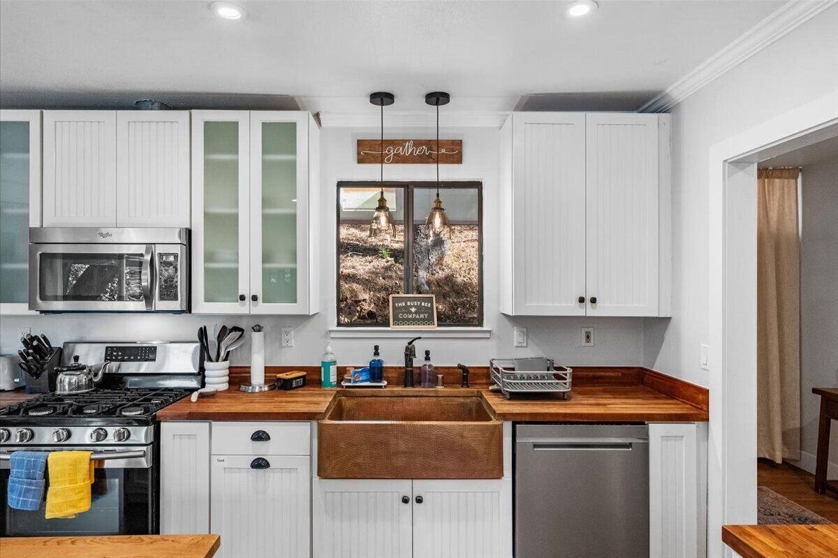 A kitchen with white cabinets, a stainless steel stove, a microwave, and a wooden countertop.