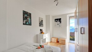 A modern bedroom with a large bed, white walls, and artwork. - Lugano Bay View Due with Balcony for 4, Cademario, Switzerland (Cademario)
