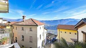 A residential area with buildings, a clear sky, and mountains in the background. - Lugano Bay View Due with Balcony for 4, Cademario, Switzerland (Cademario)