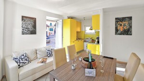 A modern living room with a sofa, dining table, and chairs. There is a kitchen in the background with yellow cabinets. - Lugano Bay View Due with Balcony for 4, Cademario, Switzerland (Cademario)