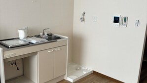 A modern kitchen with a built-in stove, sink, and a small countertop. There are wall-mounted electrical outlets and a control panel on the wall. - SakuraMandarin (Sakura)
