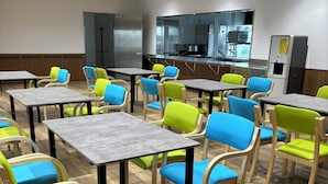 A dining area with multiple tables and chairs, a kitchen area in the background, and a wooden floor. - SakuraMandarin (Sakura)