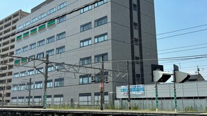A multi-story building with a grey facade, multiple windows, and visible signage. - SakuraMandarin (Sakura)