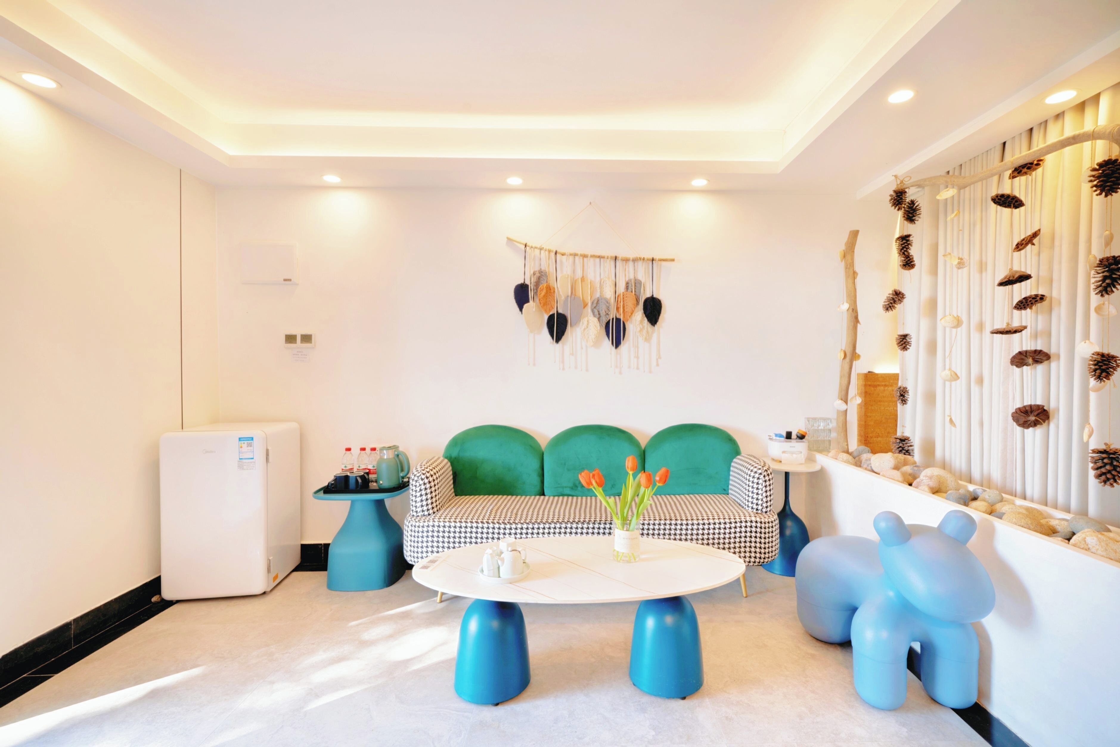 Una sala de estar moderna con un sofá a cuadros, una mesa redonda con patas azules y un adorno colgante en la pared.