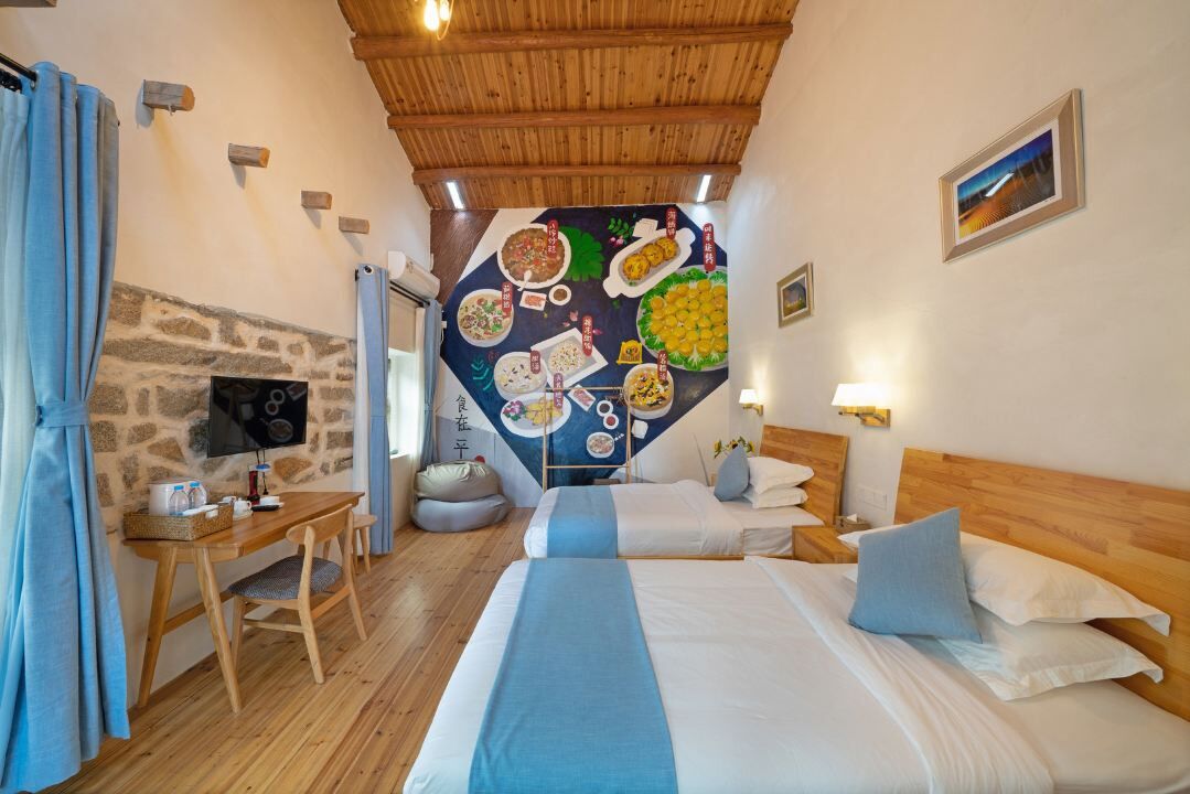Una camera accogliente con soffitto in legno, parete in pietra, letto con biancheria azzurra, una scrivania in legno e un affresco raffigurante piatti di cibo.