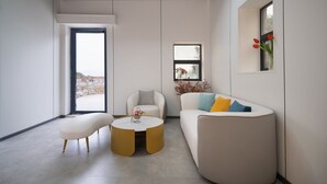 Un salon moderne comprenant un canapé, un fauteuil, un pouf et une table basse ronde.