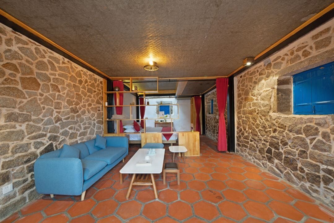 A cozy room with a stone wall, a blue sofa, a wooden coffee table, and a small dining table.
